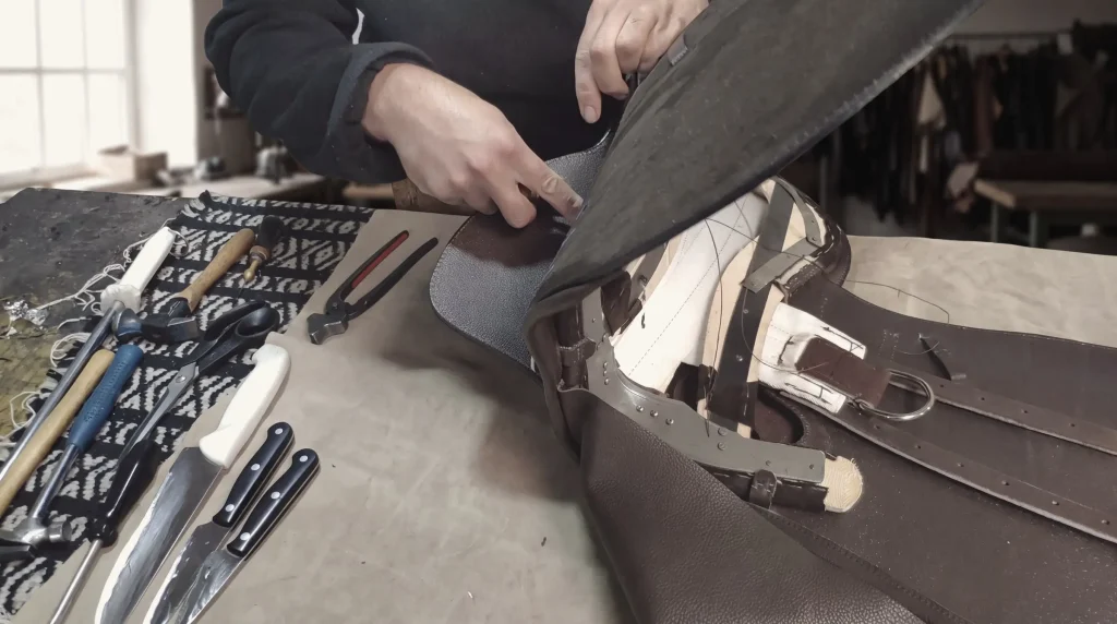 A saddler's hands drawing a leather panel over a saddle tree